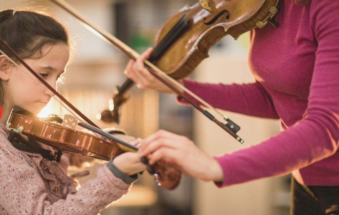 Aluna tocando violino ao lado da professora