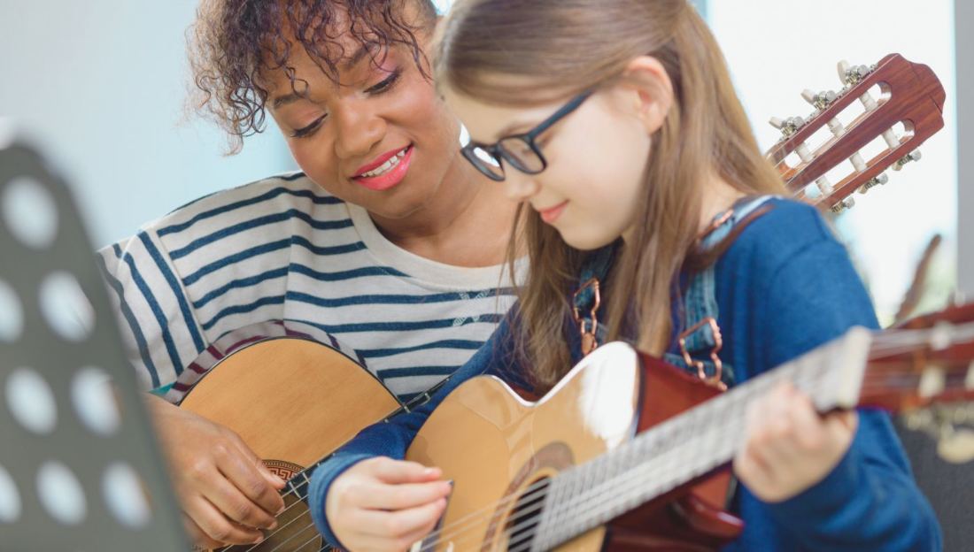 Professora e aluna tocando violão juntas em uma aula em casa